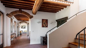 A spacious hallway with a wooden staircase, tiled flooring, and a view into a living area with a sofa and chairs.