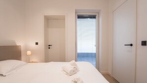 Une chambre d’hôtel avec un lit, deux portes, une lampe et une vue par une fenêtre équipée de stores.