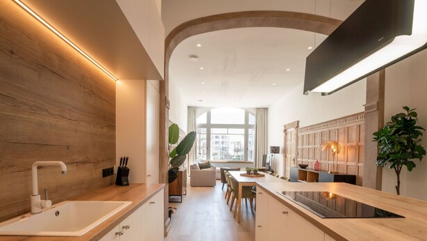 Une cuisine moderne dotée d’un îlot central, de meubles en bois et d’une grande fenêtre qui laisse entrer la lumière naturelle.