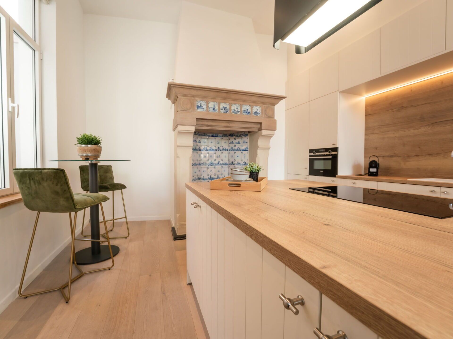 A modern kitchen with a wooden countertop, white cabinets, and a tiled backsplash. There are two bar stools and a small potted plant on the countertop.