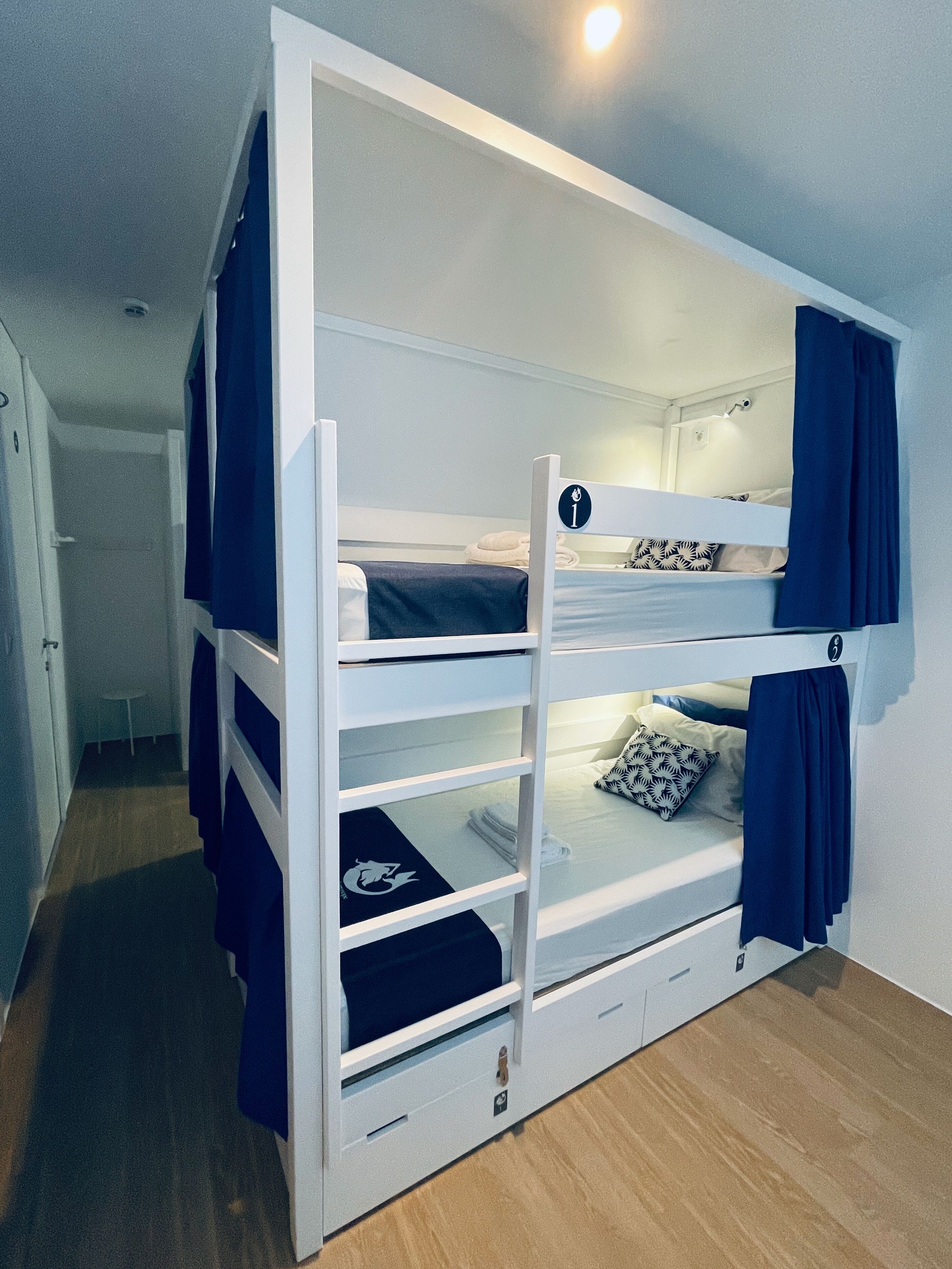 Una cama litera con una mesa de estudio plegable, una mesita pequeña y una puerta que da a otra habitación.