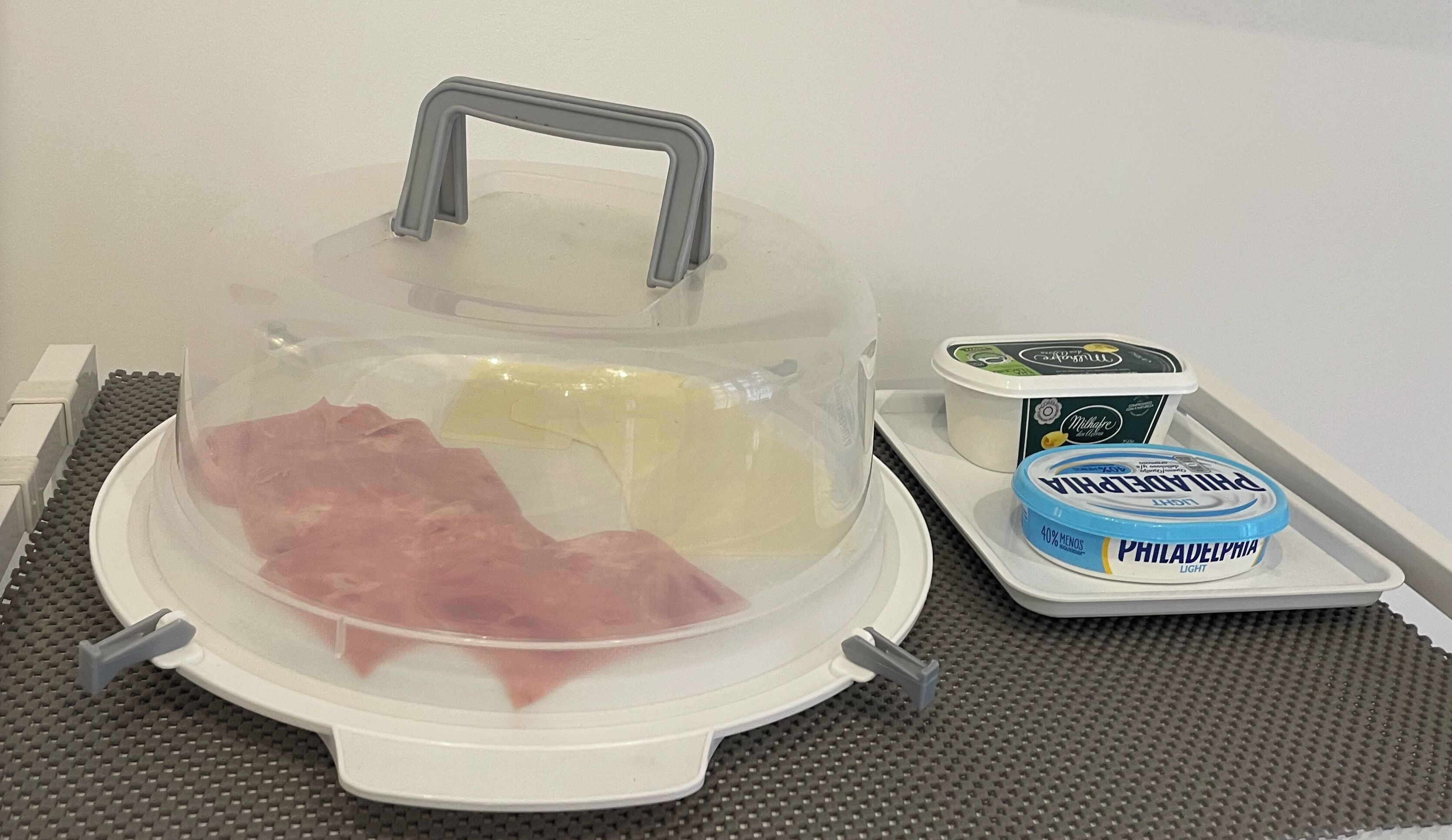 A food service station with a covered food container, a tray with a container of Philadelphia light cheese, and a container of Milkbottle yogurt.