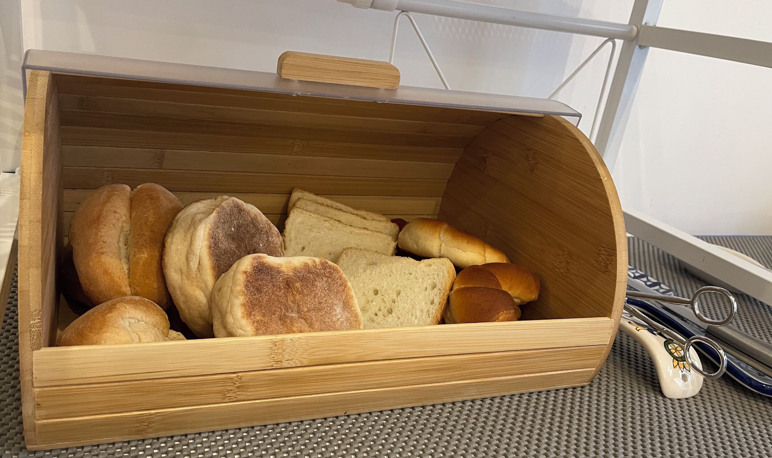 A wooden bread box with a handle, containing various types of bread.