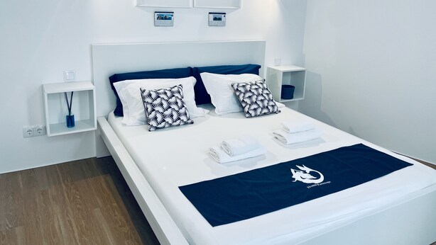 A modern hotel room with a neatly made bed, two wall-mounted nightstands, and two framed artworks above the bed. - Partenope Hostel and Suites (Angra do Heroismo)