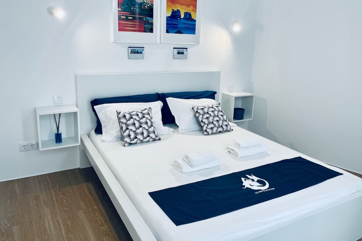 A modern hotel room with a neatly made bed, two wall-mounted nightstands, and two framed artworks above the bed.