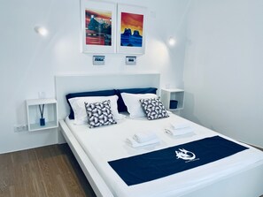 A modern hotel room with a neatly made bed, two wall-mounted nightstands, and two framed artworks above the bed. - Partenope Hostel and Suites (Angra do Heroismo)