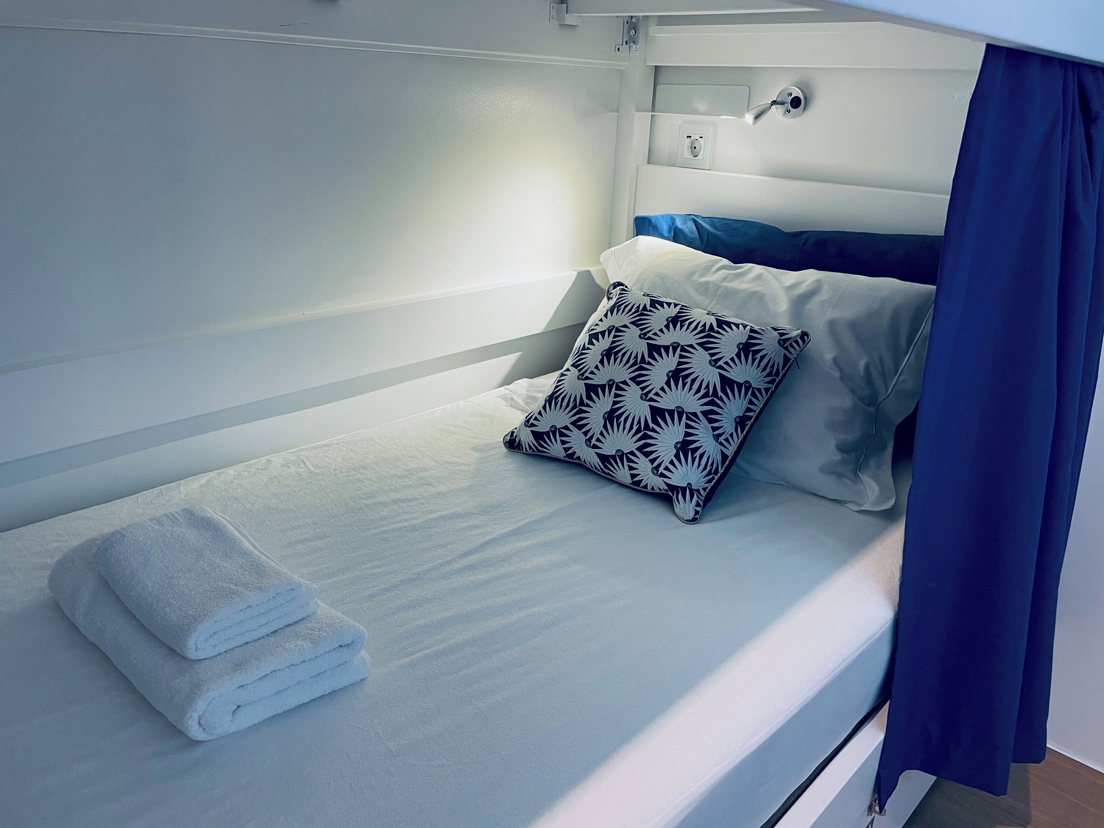 Un lit simple avec un matelas blanc, un oreiller à motifs bleus et blancs, et une serviette blanche pliée.