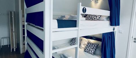A bunk bed with a white frame and blue curtains, a small stool, and a door in the background.
