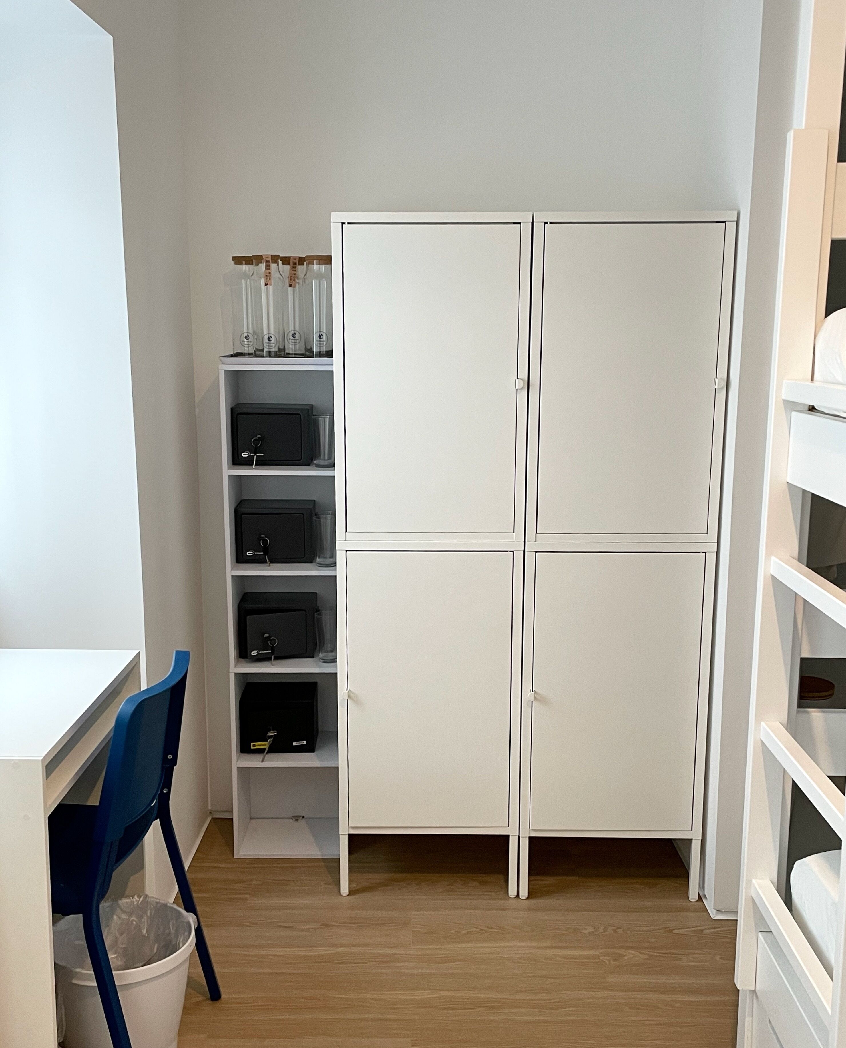 Een kamer met een wit bureau, een blauwe stoel en een witte garderobe met planken.