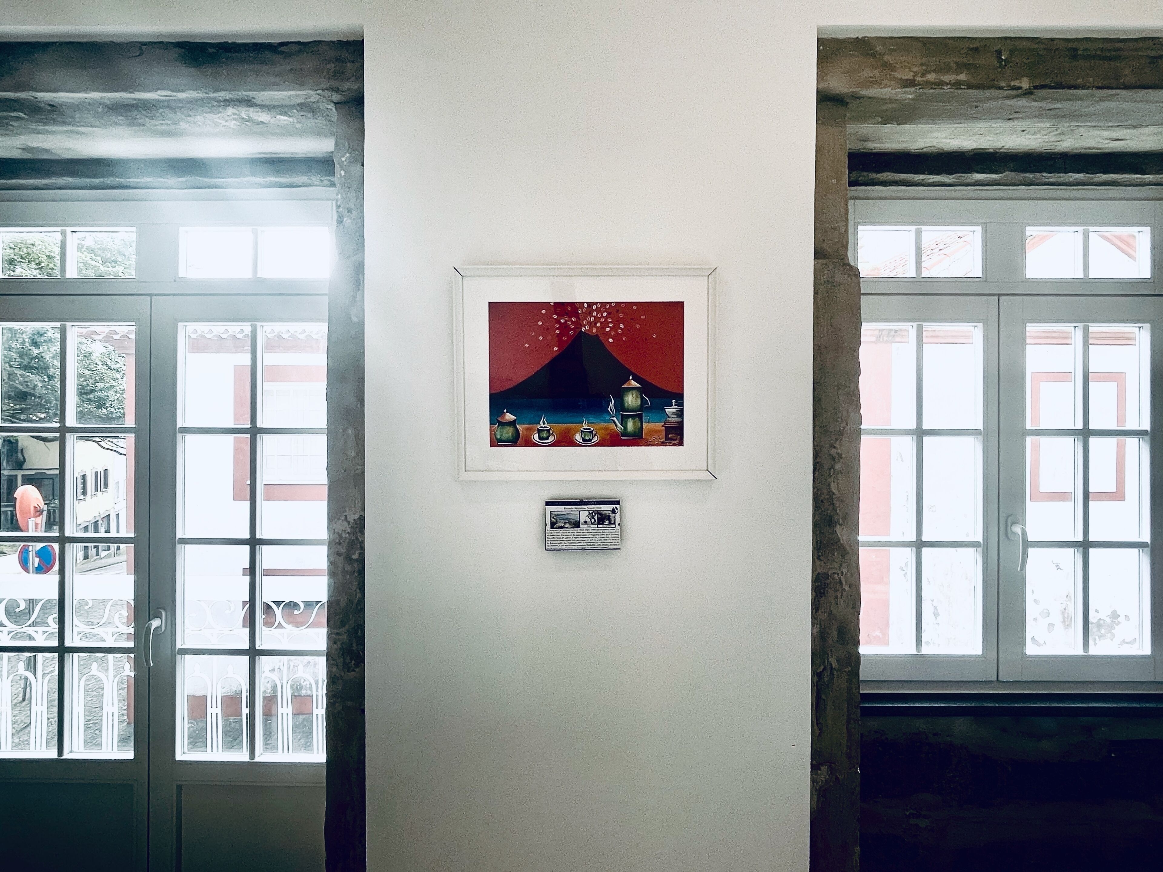 Un pasillo con una obra enmarcada en la pared, una placa debajo y una puerta con un ventanal.