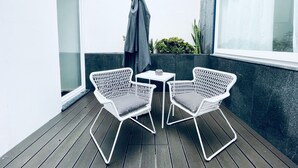 A balcony with two white wicker chairs and a small table, a grey umbrella, and a view of the building's exterior. - Partenope Hostel and Suites (Angra do Heroismo)
