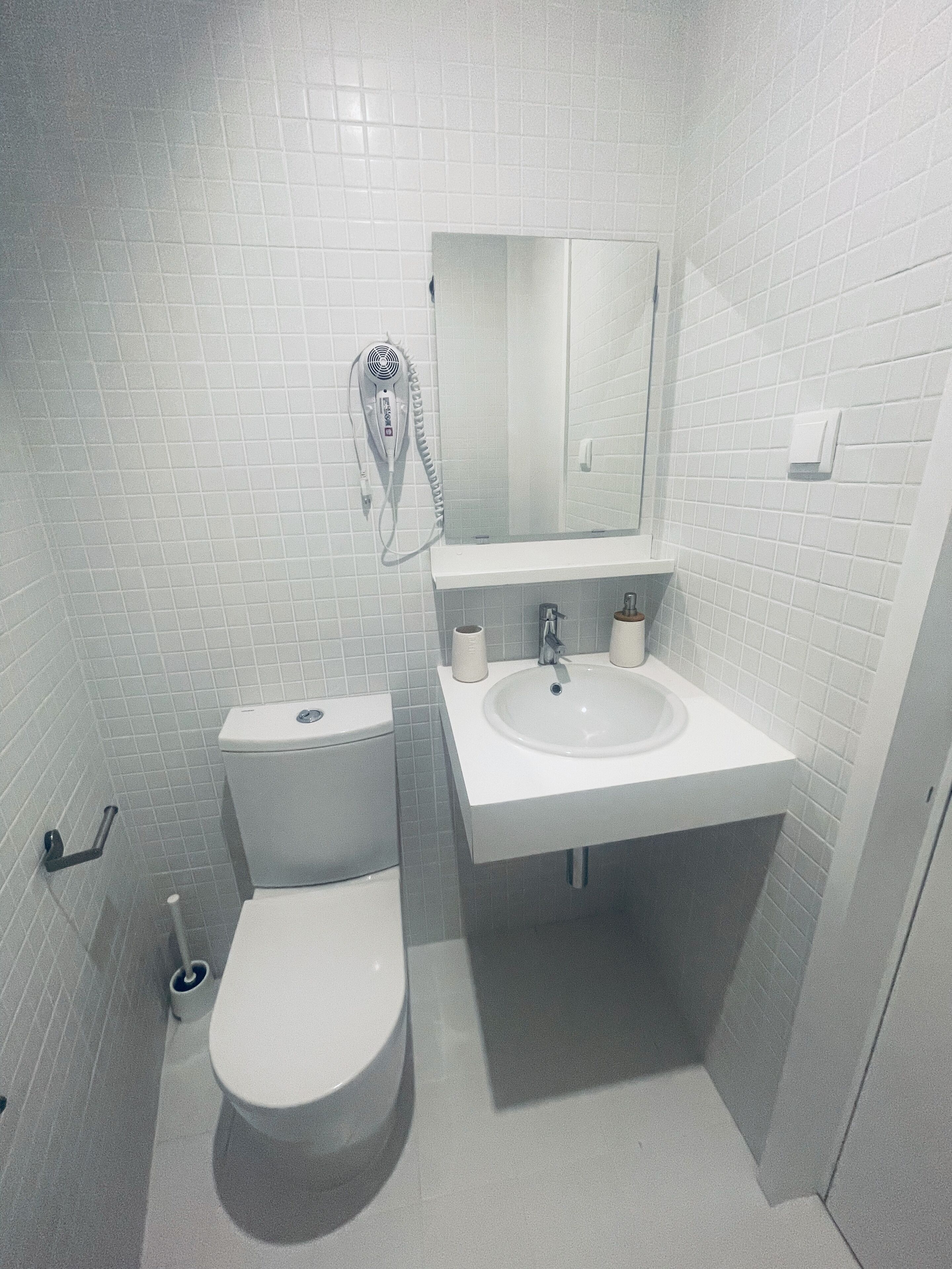 Et badeværelse med toilet, håndvask og en hårtørrer fastgjort på væggen.