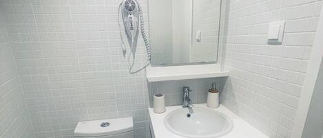Et badeværelse med toilet, håndvask og en hårtørrer fastgjort på væggen.