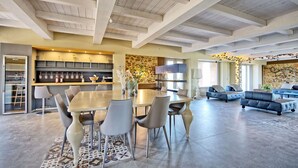 A spacious living area with a dining table, chairs, a sofa, and a coffee table. There is a kitchen area with shelves and a stone accent wall. - Stunning private villa for 12 people with WIFI, private pool, A/C, TV, patio and panoramic view (Villamagna)