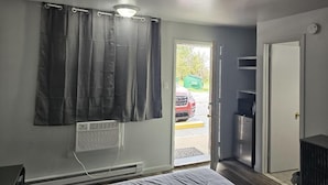 A room with a bed, a heater, a door leading outside, and a small shelf unit. - Motel 81 (Dalton)
