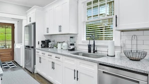 Una cocina moderna con armarios blancos, encimera de granito, lavavajillas integrado y una ventana con persianas.