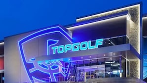 Un edificio moderno con un llamativo letrero de neón que dice "TOPGOLF" y una escalera que lleva a la entrada.