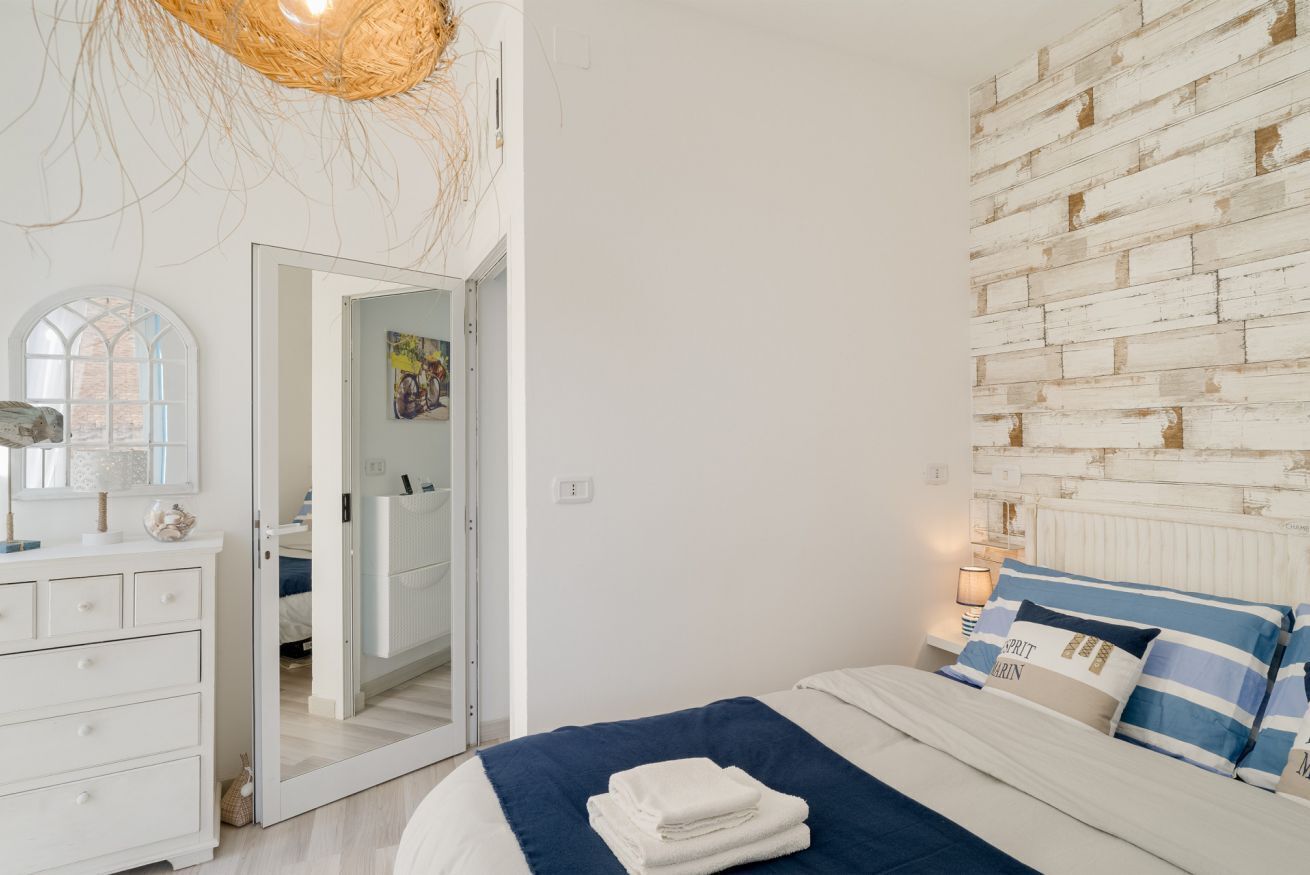 Une chambre à coucher comprenant un lit, une commode, un miroir, un mur avec un motif texturé et une porte donnant sur une autre pièce.