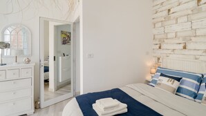 A bedroom with a bed, a dresser, a mirror, a wall with a textured pattern, and a door leading to another room.