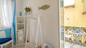 A room with a white chair, a white shelf with baskets, a drying rack, and a balcony with a table and chairs.