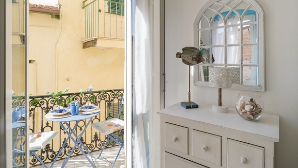 A balcony with a table set for two, a white dresser with a mirror, and a window with a decorative frame.