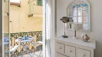 Un balcone con un tavolo apparecchiato per due, un comò bianco con uno specchio e una finestra con cornice decorativa.