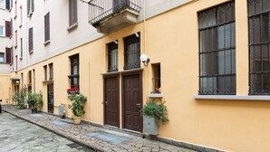 A narrow cobblestone street lined with yellow buildings, each with a brown door and windows with metal bars. - GuestHost - Apartment on 2 levels Milan-Crocetta M3! (Milano)