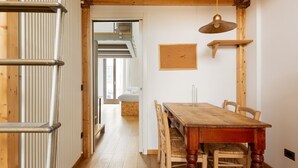 A wooden interior with a dining table, chairs, a hanging light fixture, and a corkboard on the wall. - GuestHost - Apartment on 2 levels Milan-Crocetta M3! (Milano)