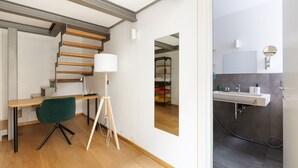 A modern room with a wooden desk, a green chair, a floor lamp, a mirror, and a bathroom with a sink and mirror. - GuestHost - Apartment on 2 levels Milan-Crocetta M3! (Milano)