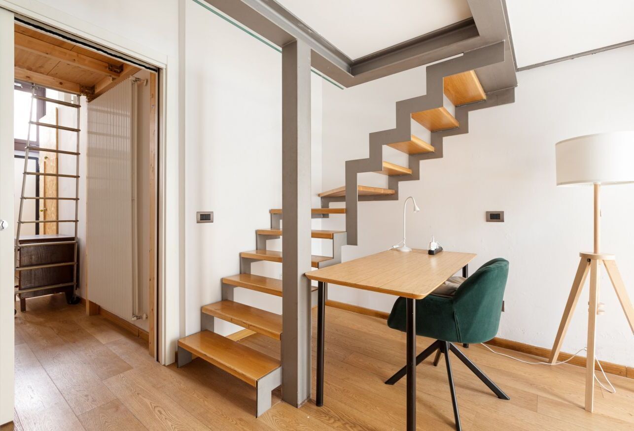 A modern interior with a wooden staircase, a dining table with chairs, and a floor lamp.