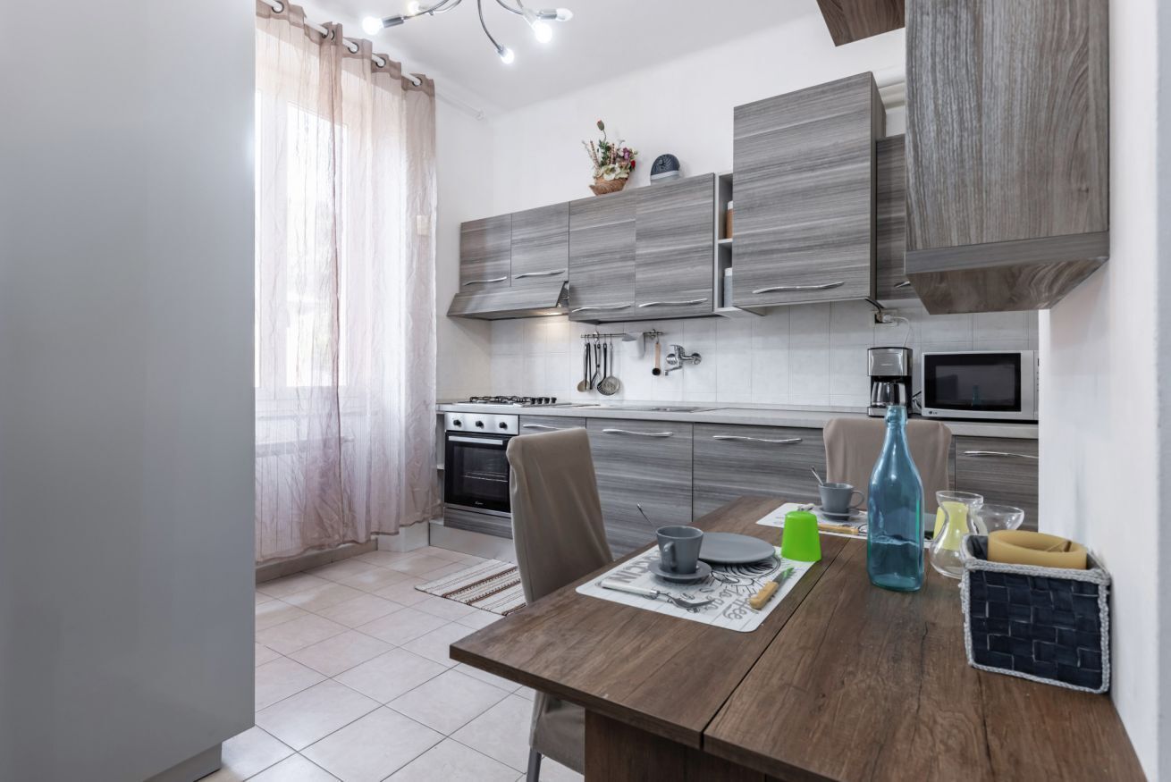 Una cocina moderna con armarios grises, una mesa de comedor con un posavasos y una botella azul.