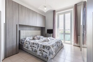 A bedroom with a large bed, a television, a balcony with curtains, and a city view. - GuestHost - Comfortable apartment of about 70 sqmt ideal for 4 people is located in the western area of the city about 1 km from the central station of La Spezia, 1500 m from the departure of the boats for all the locations of the Gulf of Poets: Lerici P (La Spezia)