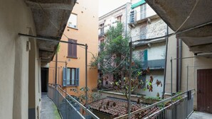 A courtyard with a small tree, a metal fence, and a tiled floor.