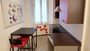A compact kitchen with a dining area, a window with curtains, and a painting on the wall.