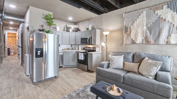 A modern kitchen with stainless steel appliances, grey cabinets, and a dining area with a grey sofa and a coffee table. - Belle Plain Inn Rustic Refuge (Baird)