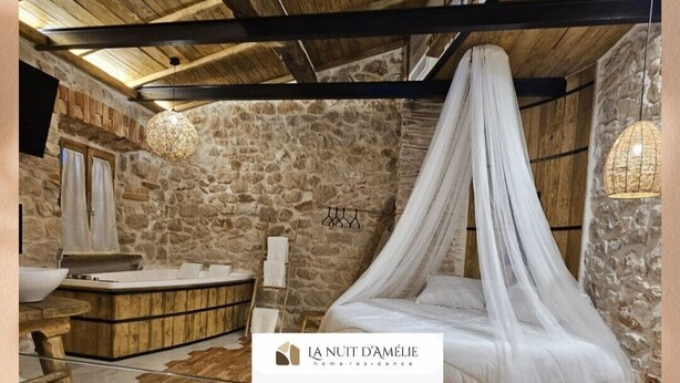 Un dormitorio rústico con pared de piedra, vigas de madera en el techo, una cama con dosel y chimenea de piedra.