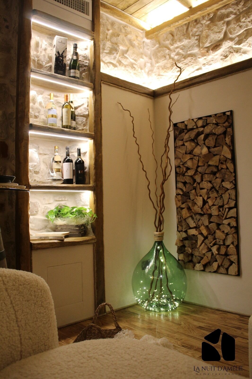 Ein Zimmer mit einer Holzhilfe, auf der Weinflaschen stehen, einer grünen Vase mit Zweigen und einem Wandbild.