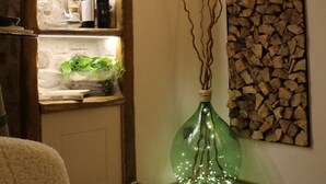 Una habitación con un estante de madera que muestra botellas de vino, un jarrón verde con ramas y una obra de arte en la pared.