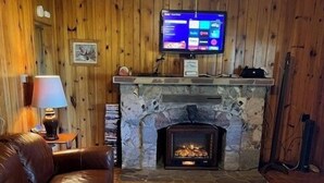 Tunnelmallinen olohuone, jossa on kivinen takka, puuseinät, nahkasohva ja seinälle asennettu televisio.