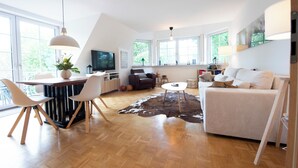 A modern living room with a wooden floor, a dining area with chairs, a sofa, a coffee table, and a TV. - Cozy heath idyll in the countryside (Schneverdingen)