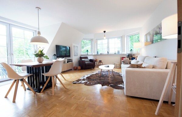 A modern living room with a wooden floor, a dining area with chairs, a sofa, a coffee table, and a TV. - Cozy heath idyll in the countryside (Schneverdingen)
