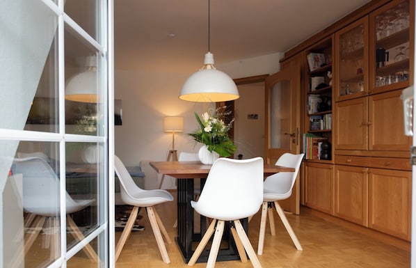 Un comedor con una mesa de madera, sillas blancas, una lámpara colgante y armarios de madera con puertas de cristal.