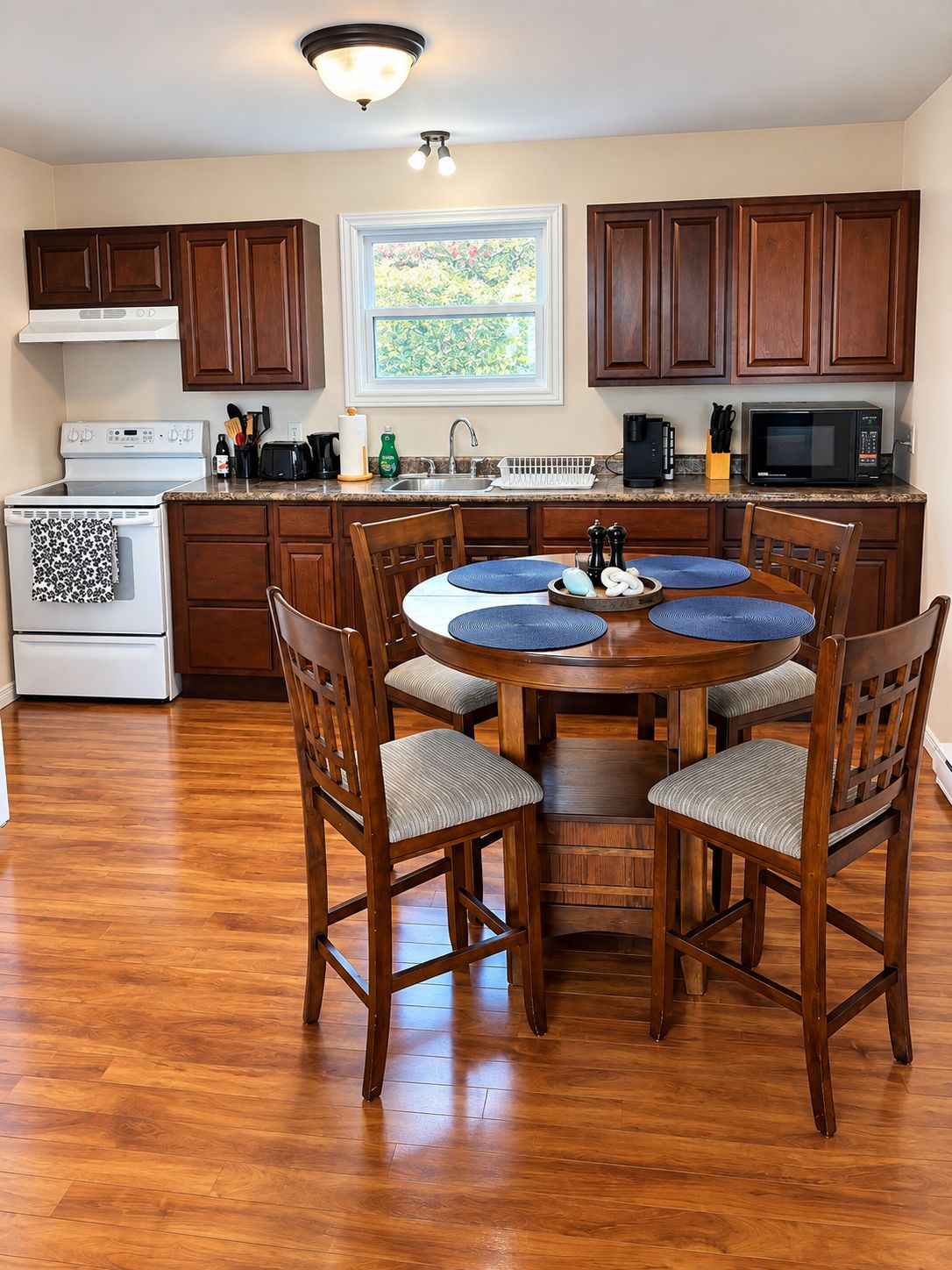 A kitchen with wooden cabinets, a stove, a microwave, and a dining table with chairs.