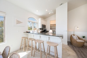 A modern kitchen with a central island, bar stools, and a wicker chair.