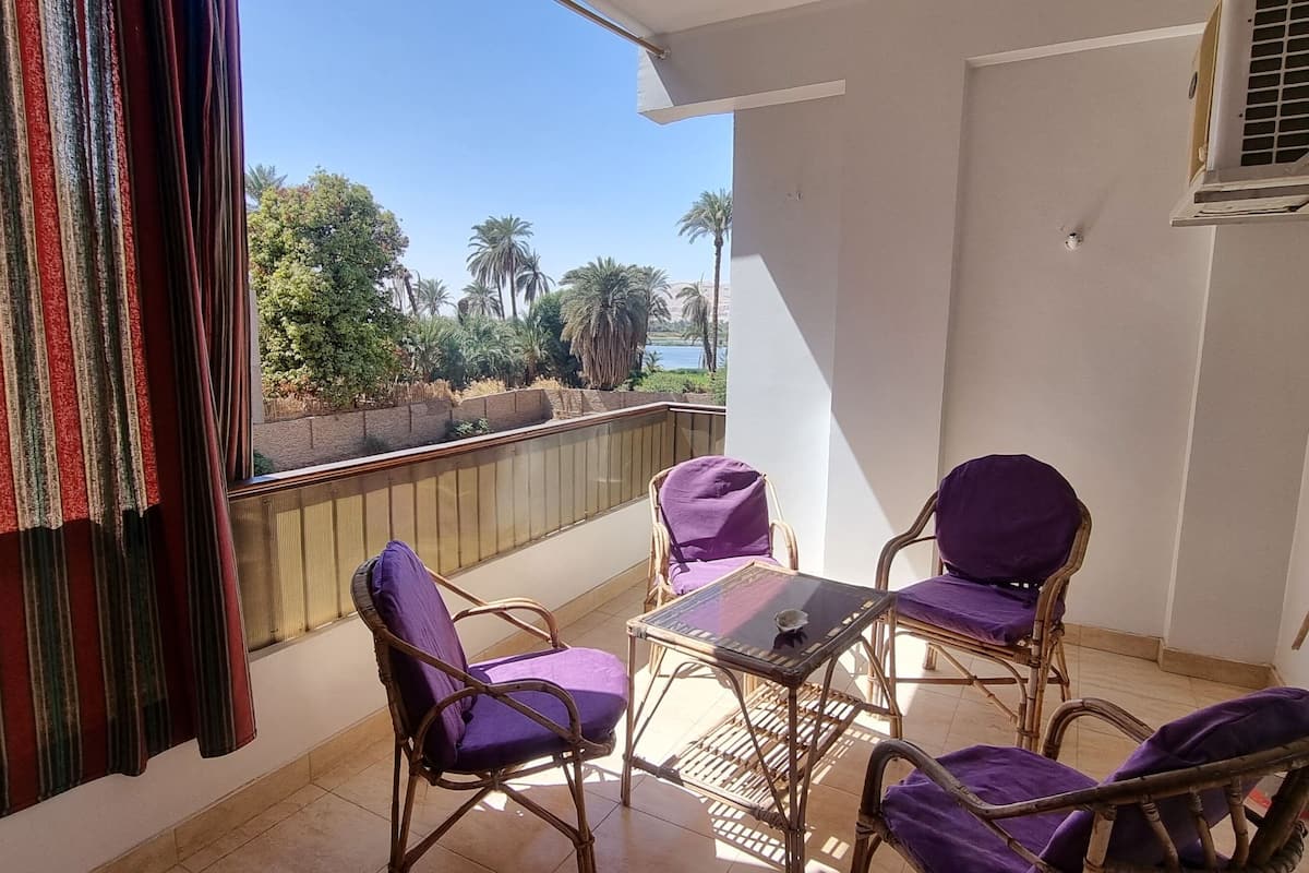 Ein Balkon mit Korbmöbeln und Blick auf Palmen und ein Gewässer.