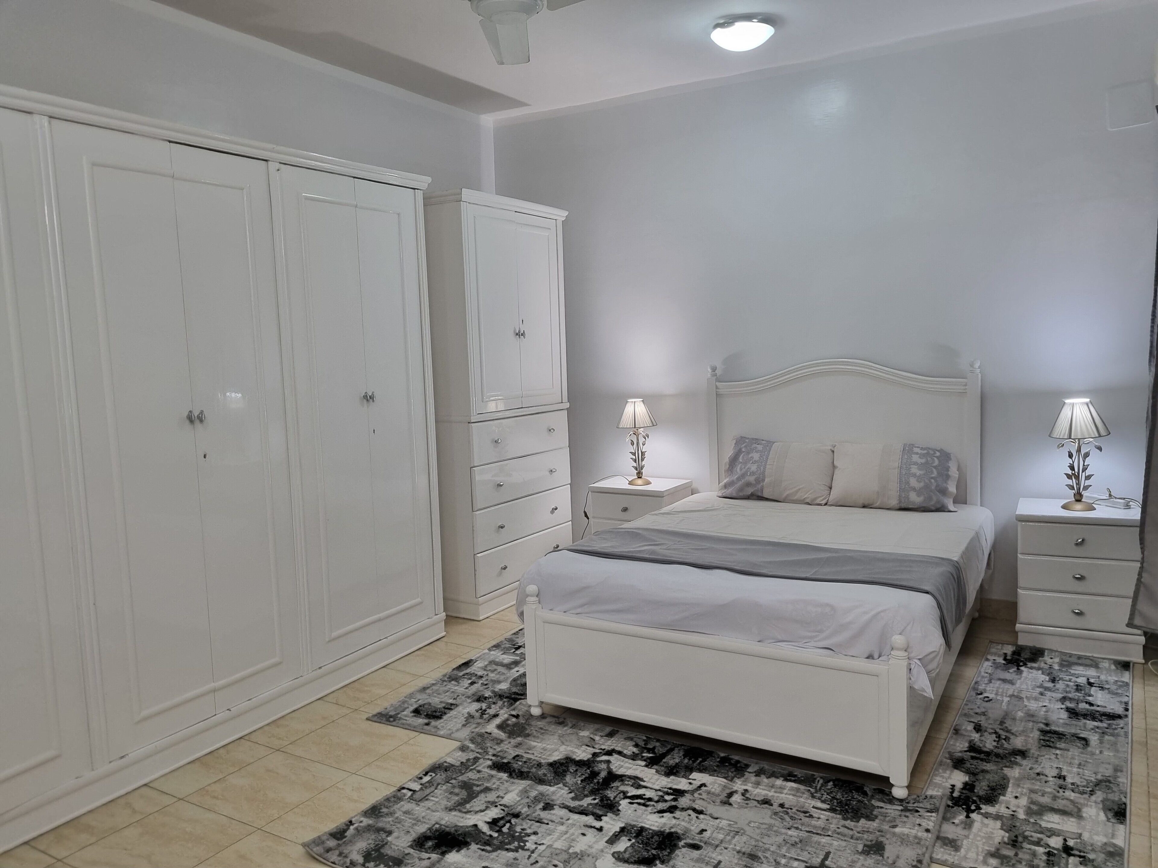 Un dormitorio con cama, mesitas de noche, un armario y una alfombra estampada.