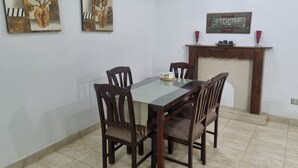 Un comedor con una mesa de vidrio, sillas de madera y dos cuadros en la pared.