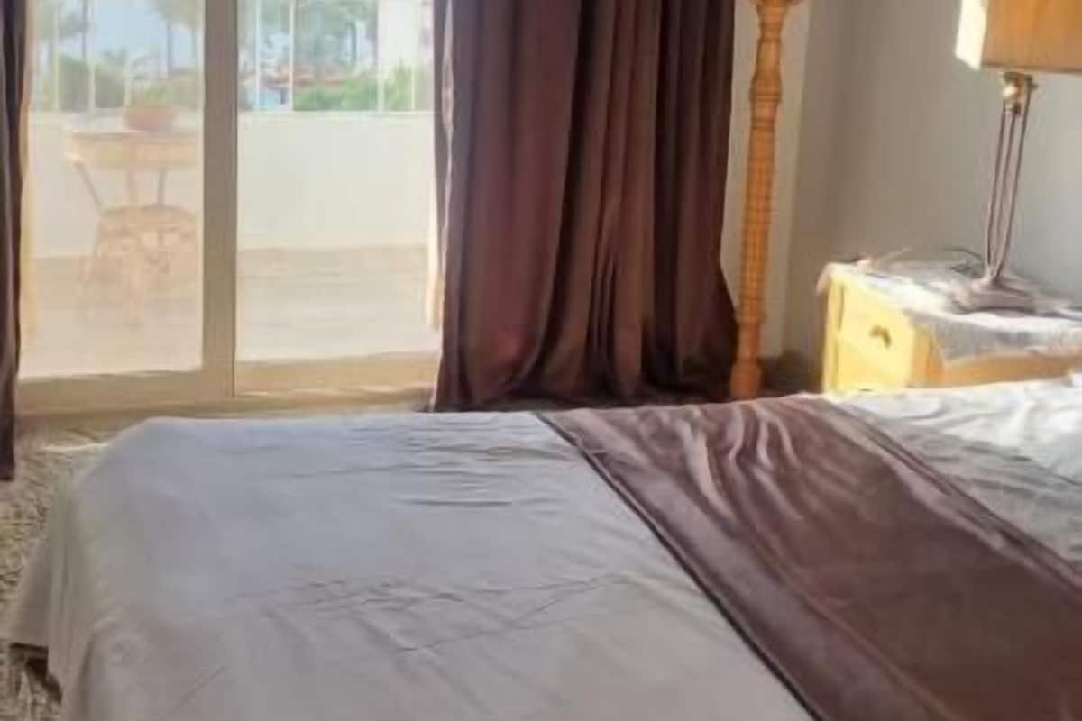 Ein Hotelzimmer mit einem Bett, einer Lampe, einem Holzanzughalter und Blick auf einen Balkon mit Tisch und Stühlen.