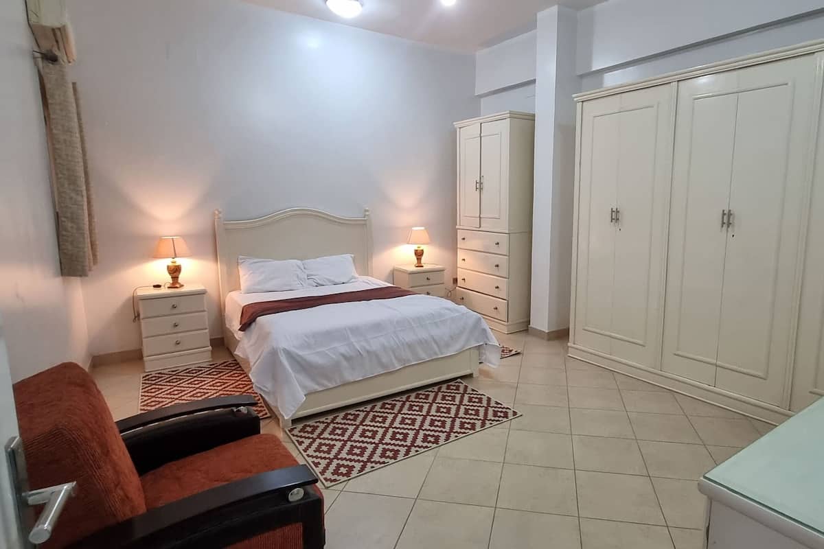 Ein Schlafzimmer mit einem Bett, zwei Nachttischen mit Lampen, einem Kleiderschrank, einem Sessel und einem kleinen Tisch.