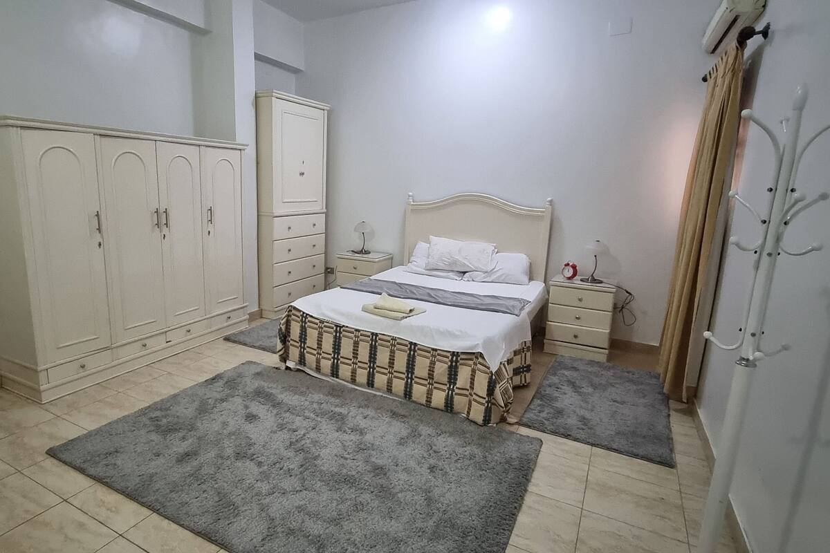 Ein Schlafzimmer mit Bett, Kleiderschrank, Stuhl und Kleiderhaken.